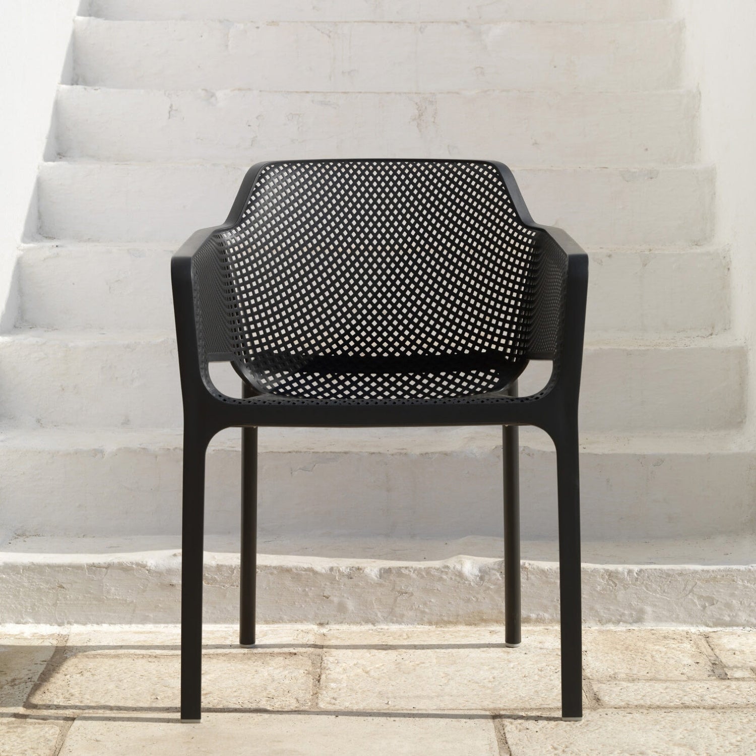 A single black Replica Net Armchair placed against a white staircase background, highlighting its stylish aesthetic.