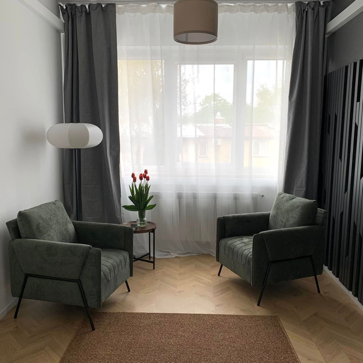 Two Kreslo Green Armchairs in a bright living space with tulips on a side table.
