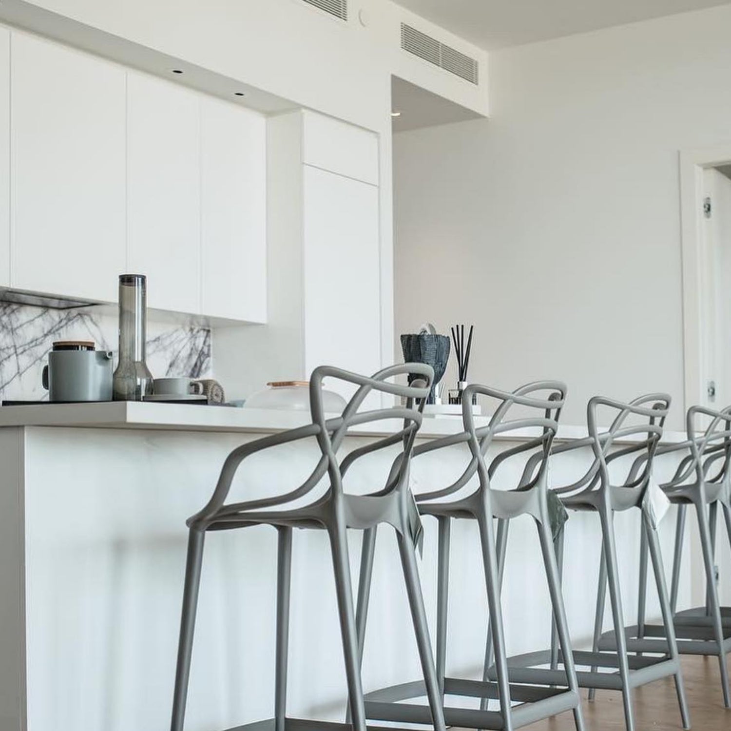 A row of grey Replica Masters Bar Stools at a white kitchen counter, showing how they fit seamlessly into a modern home.