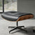 A stylish Eames ottoman featuring a black leather seat and elegant wooden legs, perfect for adding sophistication to any room.