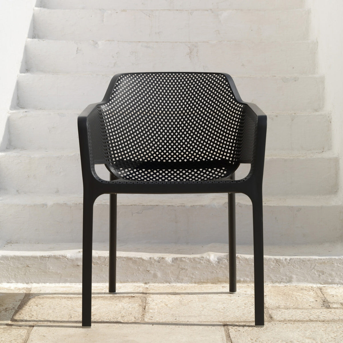A single black Replica Net Armchair placed against a white staircase background, highlighting its stylish aesthetic.