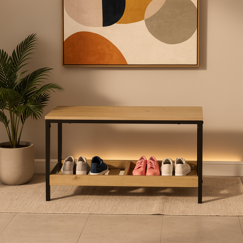 A modern wooden entryway shoe bench with a light natural wood top and shelf, supported by a black metal frame. The bench is styled in a home entryway with various shoes on the shelves, a potted plant on the left, and a framed abstract art print on the beige wall behind it.