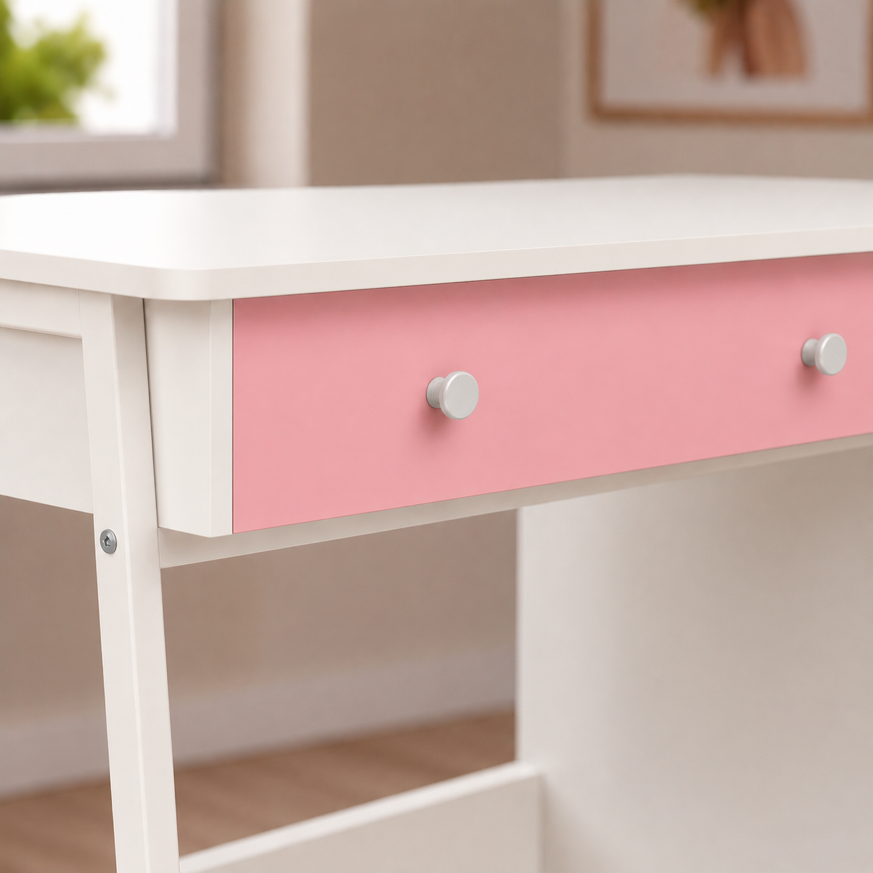 A close-up of a white desk with a single pink drawer featuring two round silver knobs, set in a softly lit room.